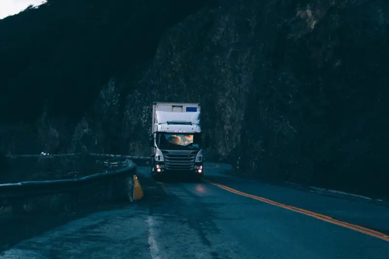 Witte vrachtwagen met gesloten laadbak komt bij schemering over een bergweg aanrijden